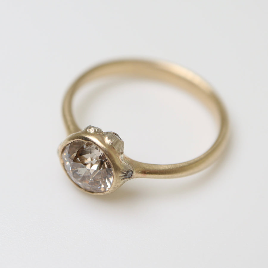 A 1.07ct Old Mine Cut diamond ring. The diamond is set in 10k gold with a tapered 10k gold band The setting is encrusted with bright sterling silver barnacles. The barnacles are inlaid with tiny diamonds. The ring is viewed from the side and is on a white background.