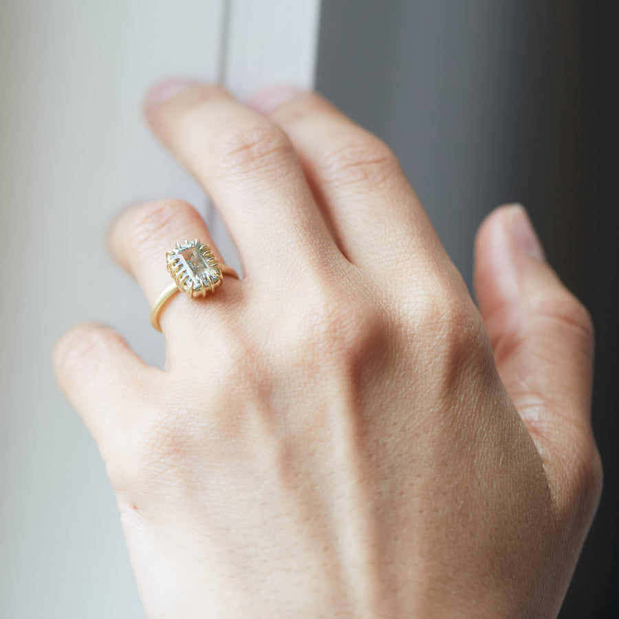 A 2.35ct Tourmaline ring set in 18k gold with a gold band. The Tourmaline is a stormy gray-blue. The Tourmaline is fastened to the setting by 16 gold prongs. The ring is displayed on a hand.