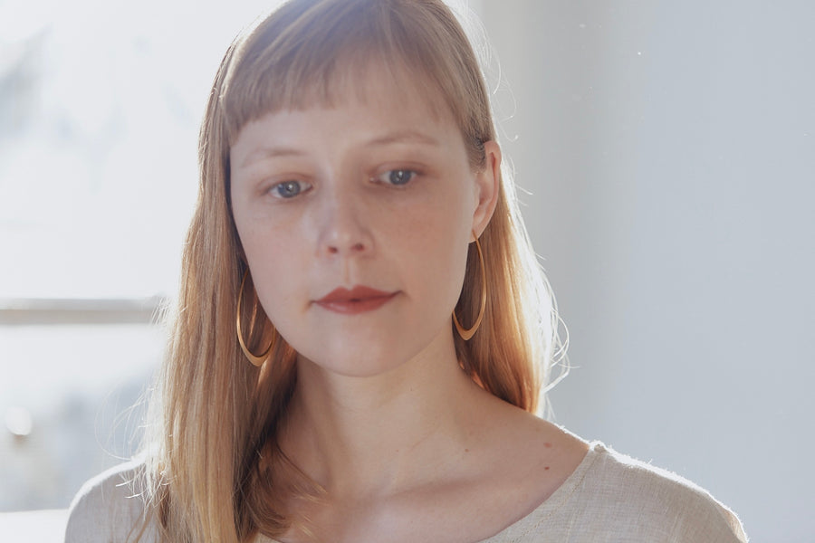 designer wearing her large facet hoops in 14k rose gold with red lips and blonde hair with bangs