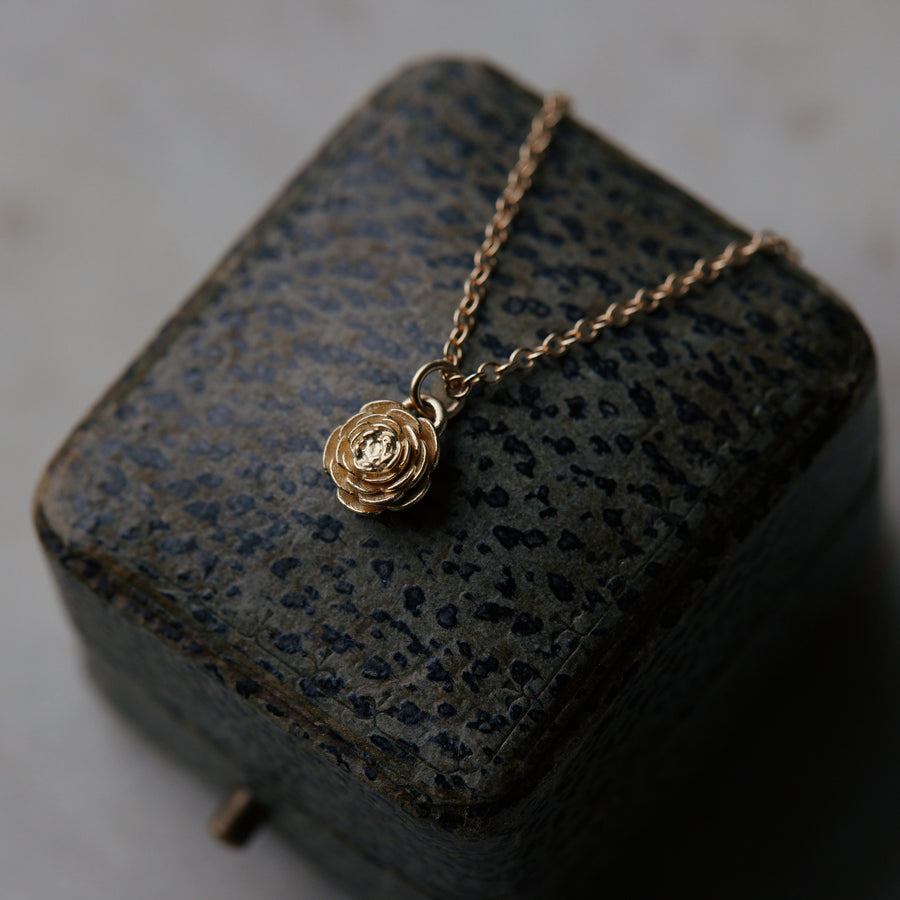 golden rose pendant necklace laying on leather jewelry box