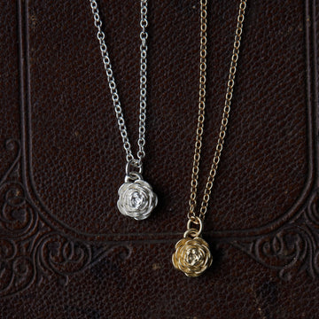 two rose pendant necklaces laying on a leather patterned book