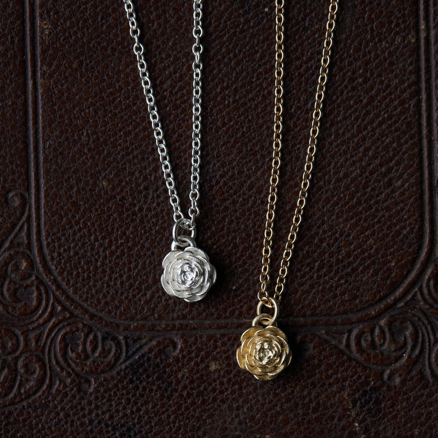 two rose pendant necklaces laying on a leather patterned book