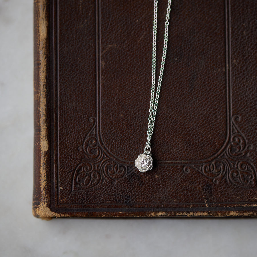 silver rose garden pendant necklace laying on leather book on marble