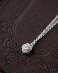 silver rose pendant necklace laying on leather book