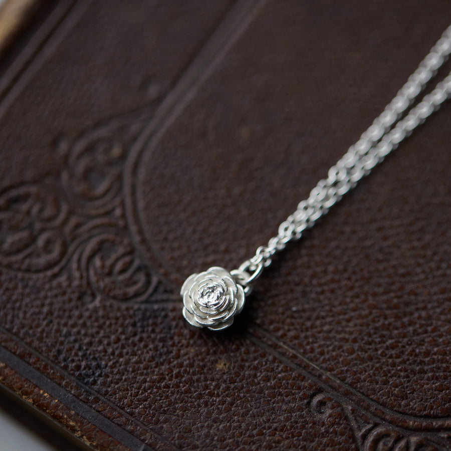 silver rose pendant necklace laying on leather book