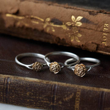 three rose sizes of silver and gold rose rings, sitting on leather books