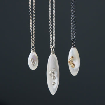 mother of pearl pendants on chains in varying metals, from bright sterling silver to oxidized silver + 14k gold combination, and in three sizes: little, medium, large.