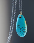 kingman turquoise pendant with inked illustration of a school of tiny fish on oxidized silver chain with gold details