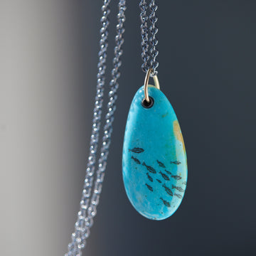 kingman turquoise pendant with inked illustration of a school of tiny fish on oxidized silver chain with gold details