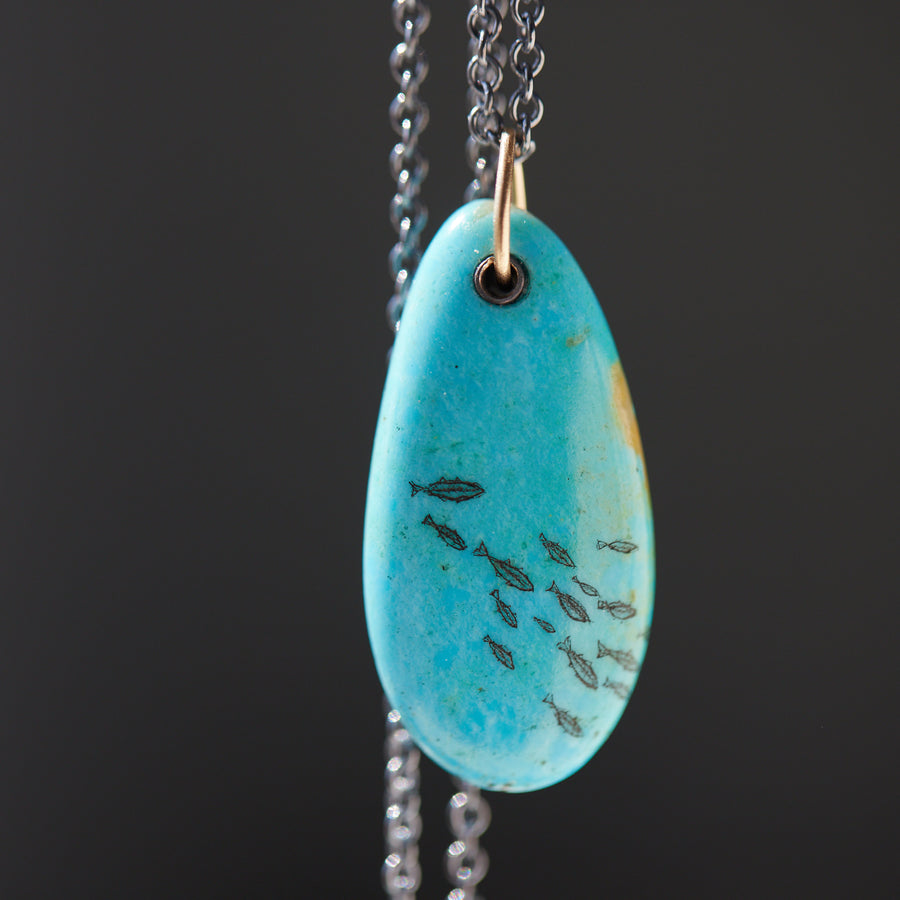 kingman turquoise pendant with inked illustration of a school of tiny fish on oxidized silver chain with gold details