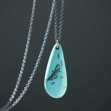 kingman turquoise teardrop bead with ink scrimshaw of codfish and little fishes. Necklace with gold and oxidized silver.