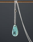 kingman turquoise pendant of scrimshaw of hand. Gold link with silver chain.