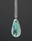 kingman turquoise pendant of scrimshaw of hand. Gold link with silver chain.