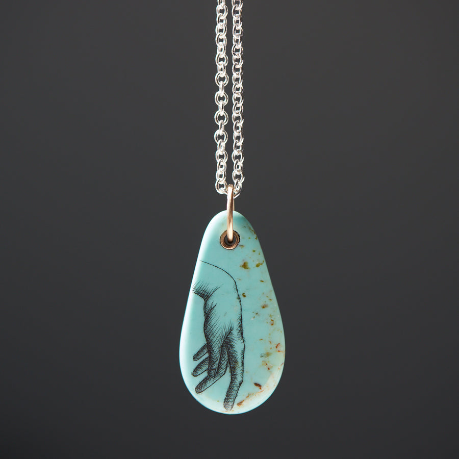 kingman turquoise pendant of scrimshaw of hand. Gold link with silver chain.