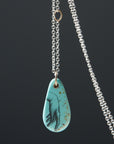 kingman turquoise pendant of scrimshaw of hand. Gold link with silver chain.