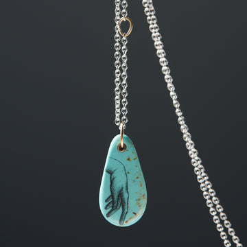 kingman turquoise pendant of scrimshaw of hand. Gold link with silver chain.