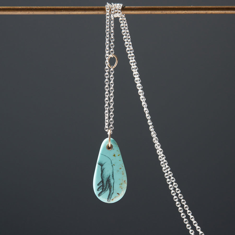 kingman turquoise pendant of scrimshaw of hand. Gold link with silver chain.