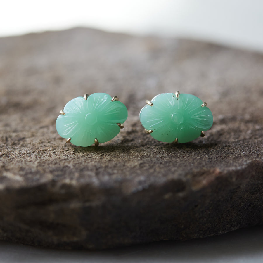 13.06ct Carved Chrysoprase Studs on a dark stone background. The Carved Chrysoprase is set with six 14k gold prongs. The Carved Chrysoprase is oval shaped with a carved flower motif. One of the studs is in profile to show the 14k gold post and bright silver stone seat.