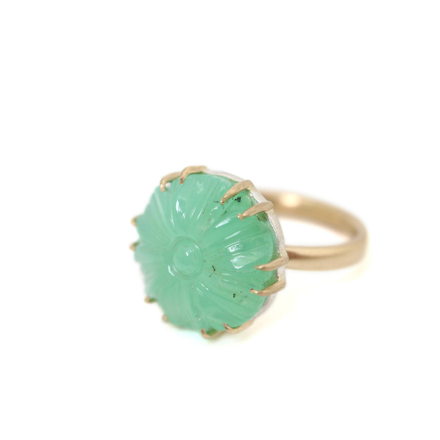 9.39ct Carved Chrysoprase Vanity Ring on a white background. The ring is viewed from it's right side slightly below eye level. The gold prongs transition into the bright silver of the stone seat. The top right and middle have black speckles. 