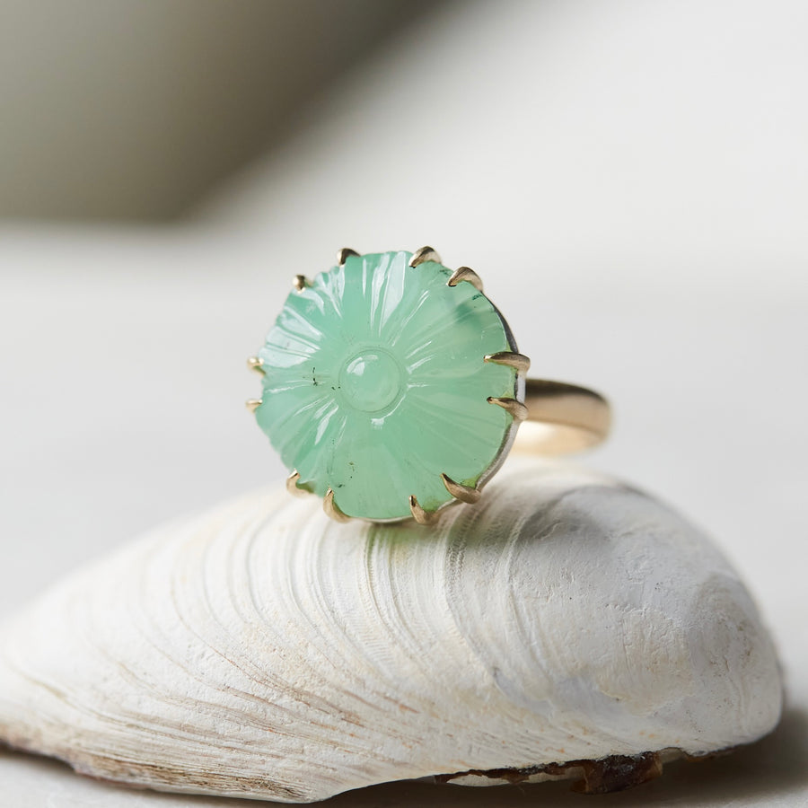 9.39ct Carved Chrysoprase Vanity Ring balanced on a white shell with a neutral background. The Chrysoprase is carved like a flower with twelve gold prongs securing it to it's setting. The Chrysoprase has a few small black speckles on it's left side.