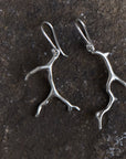 A pair of bright sterling earrings with silver coral shaped dangles. The earrings are similar but organically mismatched. 