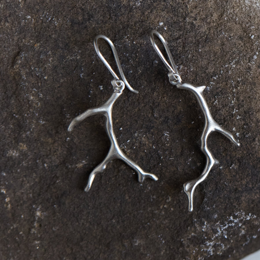 A pair of bright sterling earrings with silver coral shaped dangles. The earrings are similar but organically mismatched. 