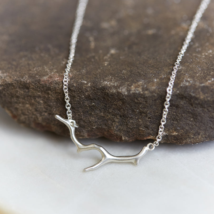 A bright sterling silver necklace with a silver coral shaped pendant. The necklace is draped on a stone.