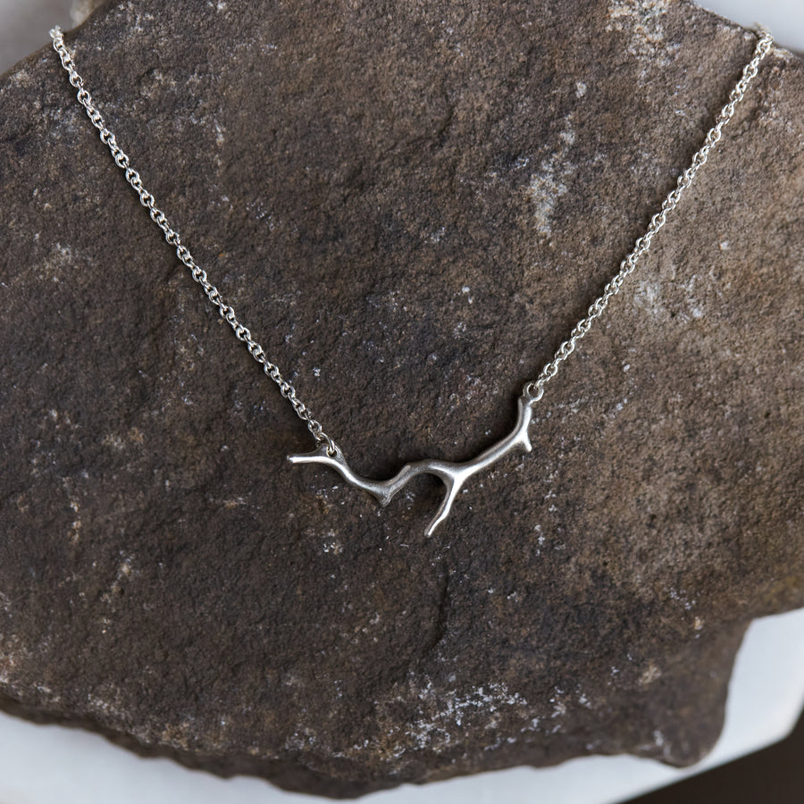 A bright sterling silver necklace with a silver coral shaped pendant. The necklace is draped on a stone.