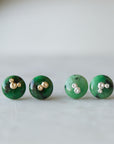 two pairs of green garnet earring studs, the left pair has gold barnacles and the right pair has silver barnacles.