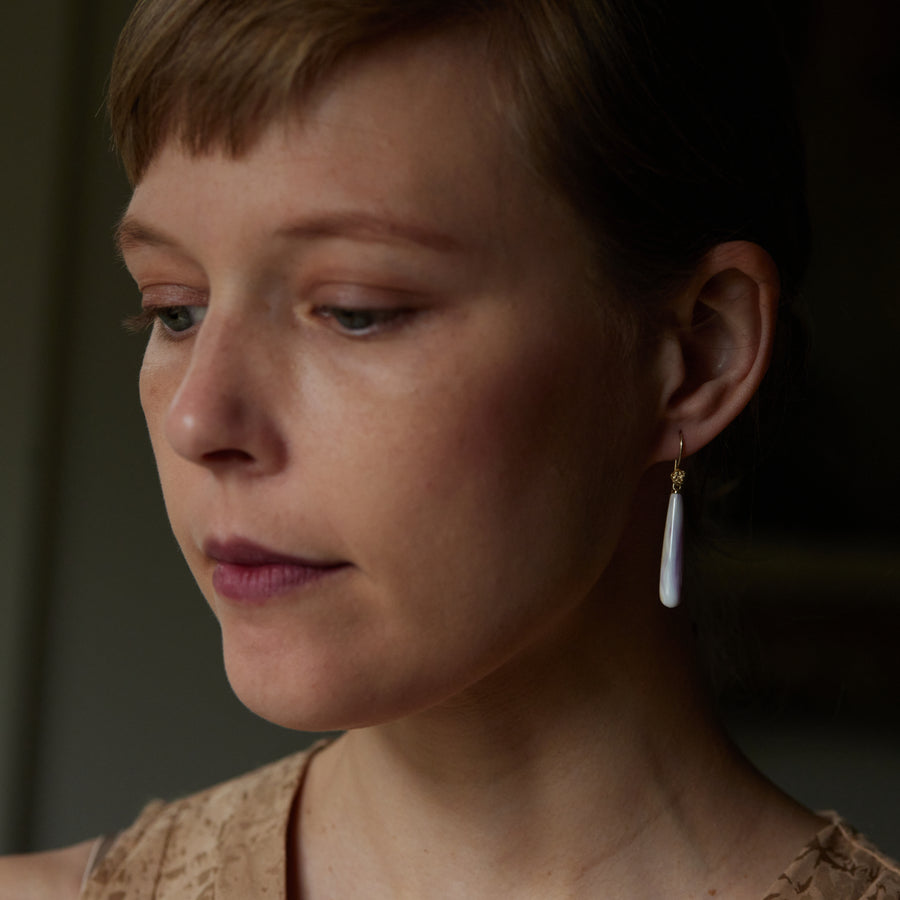 purple and white mottled quahog shell teardrops hang beneath gold ear wires with gold roses- shown on person