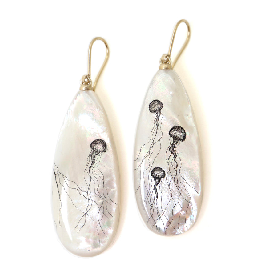 long teadrop mother of pearl earrings have gold ear wires and 3 jellyfish hand etched into the surface in black ink. A 4th jellyfish is on the back of the left earring, with the tentacles reach over onto the front.