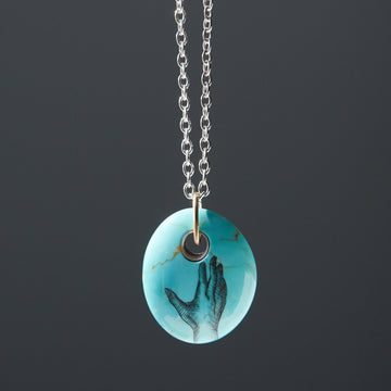 kingman turquoise bead pendant necklace on silver chain with gold bail. A scrimshaw hand is inked to the front.