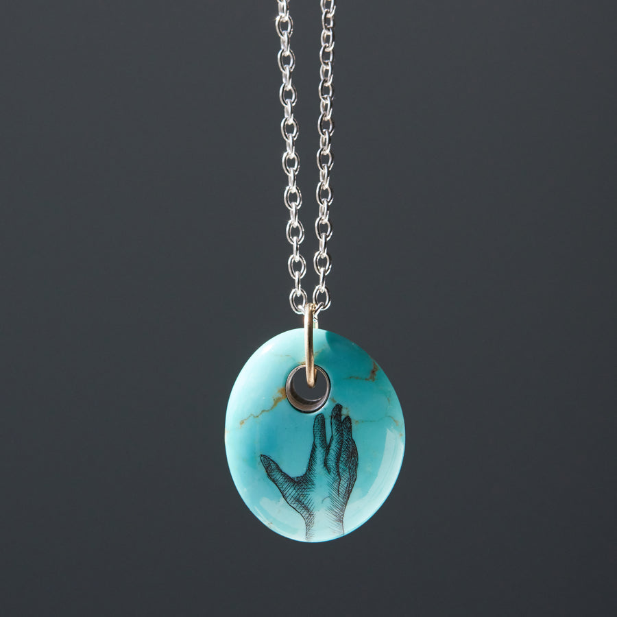 kingman turquoise bead pendant necklace on silver chain with gold bail. A scrimshaw hand is inked to the front.