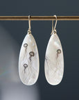 long teadrop mother of pearl earrings have gold ear wires and 3 jellyfish hand etched into the surface in black ink. A 4th jellyfish is on the back of the left earring, with the tentacles reach over onto the front.