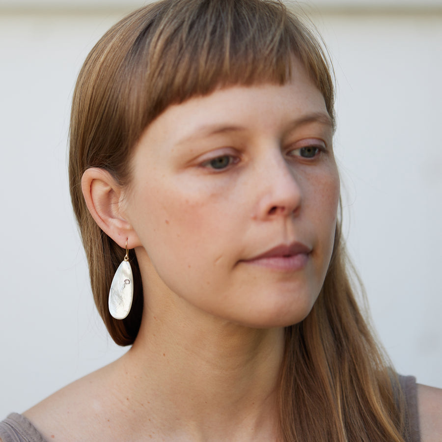 long teadrop mother of pearl earrings have gold ear wires and 3 jellyfish hand etched into the surface in black ink. A 4th jellyfish is on the back of the left earring, with the tentacles reach over onto the front.