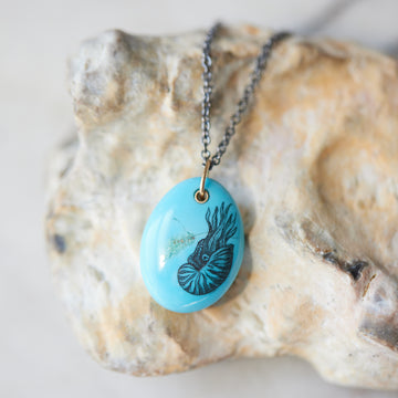 kingman turquoise pendant with inked illustration of a nautilus on oxidized silver chain with gold details