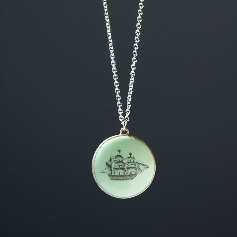 melon green round variscite cabochon is set in a gold bezel and hangs beneath a silver chain. an old whaling ship is hand-etched into the surface with black ink.