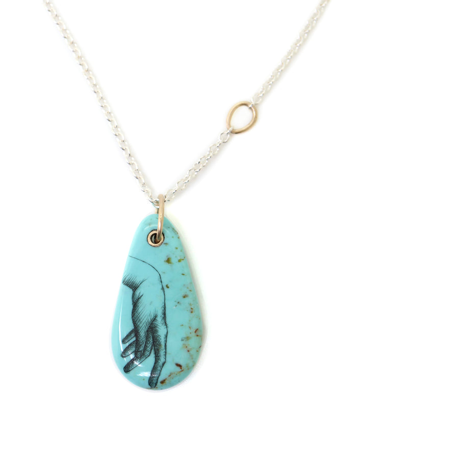 kingman turquoise pendant of scrimshaw of hand. Gold link with silver chain.