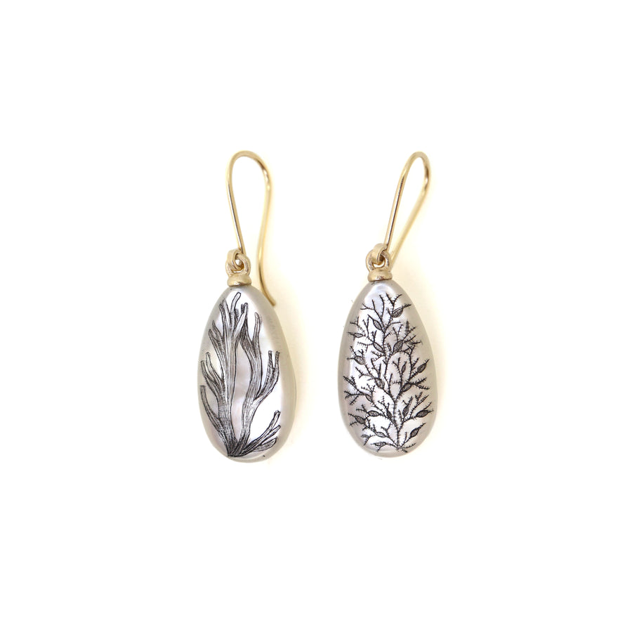 teardrops of white mother of pearl hang beneath gold ear wires. two different types of seaweed are hand etched into the surface with black ink via a method called scrimshaw.