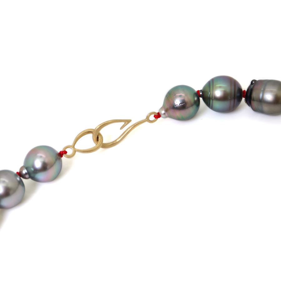 detail of necklace made from chunky grey and black tahitian pearls, strung on red silk with gold barnacles and fish hook clasp