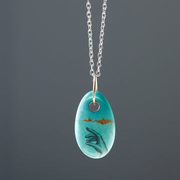 kingman turquoise bead with hand scrimshaw in ink. Pendant necklace with bright silver chain with gold egg link.