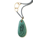 green turquoise teardrop bead with gold link and black chain. a scrimshaw hand is inked to the surface.