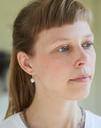 girl with bangs wearing white pearl drop earrings with gold barnacles.