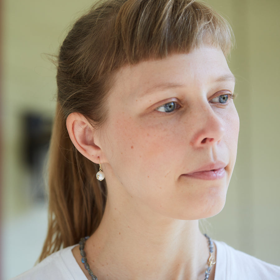 girl with bangs wearing white pearl drop earrings with gold barnacles.