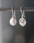 white pearl drop earrings hanging from a steel bar. The barnacles and ear wires are bright sterling silver.