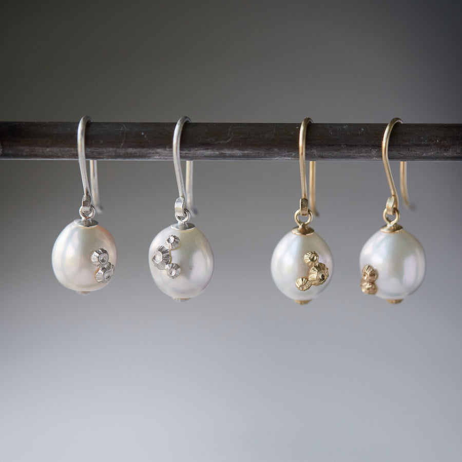 two pairs of white pearl drop earrings with barnacles. One pair on the left has silver barnacles, the pair on the right has gold barnacles.