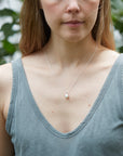 girl with blue tank top wearing a small pearl pendant necklace on a silver chain. The pendant is a white pearl with gold barnacles.