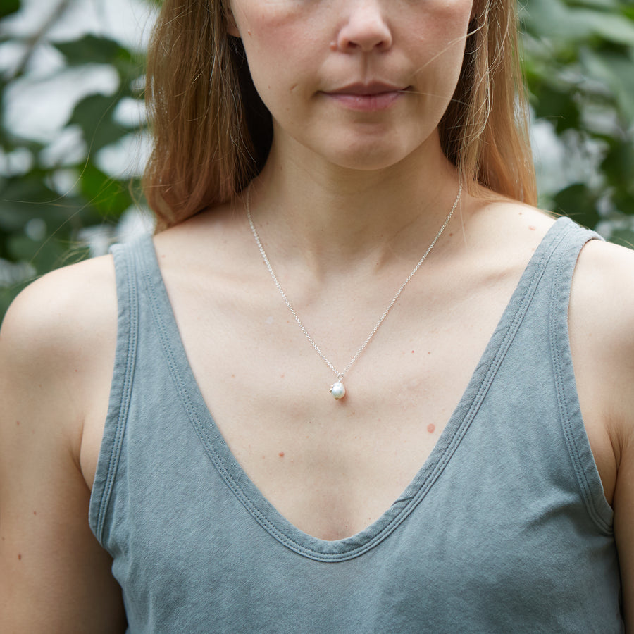 girl with blue tank top wearing a small pearl pendant necklace on a silver chain. The pendant is a white pearl with gold barnacles.